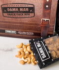 Damn, Man Snacks Snack Pack Box and a single bag opened on a table with nuts coming out of the bag