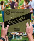 Hands holding Military Snack Box with snacks ready to eat, perfect for adventure and mission, outdoors gathering in the background