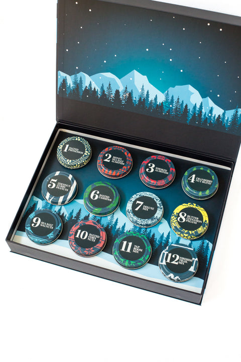 12 Days of Gourmet Nuts Winter Wonderland Selection, open calendar box displaying nut snacks with a mountain and forest background.